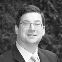 Headshot of Arthur Goldgaber, finance writer. Arthur, author of Structured Attorney Fees | Defer Taxes on Legal Fee Income, is wearing glasses and looking straight towards the center of the photo, in a shirt, tie, and coat.