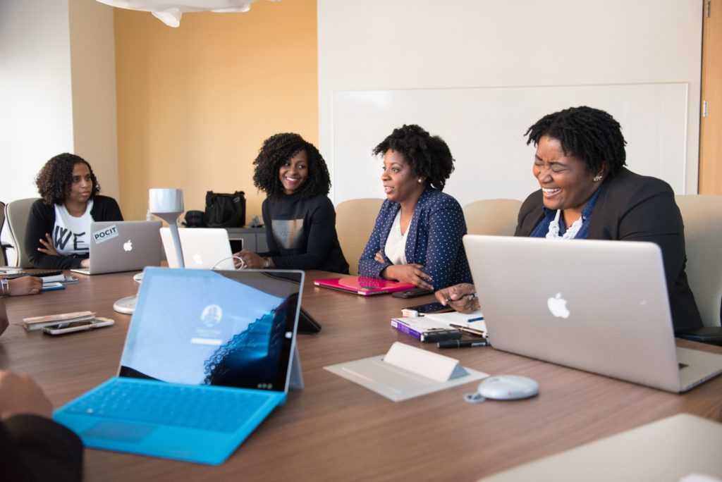 Group of black women with laptop computers at a conference table.